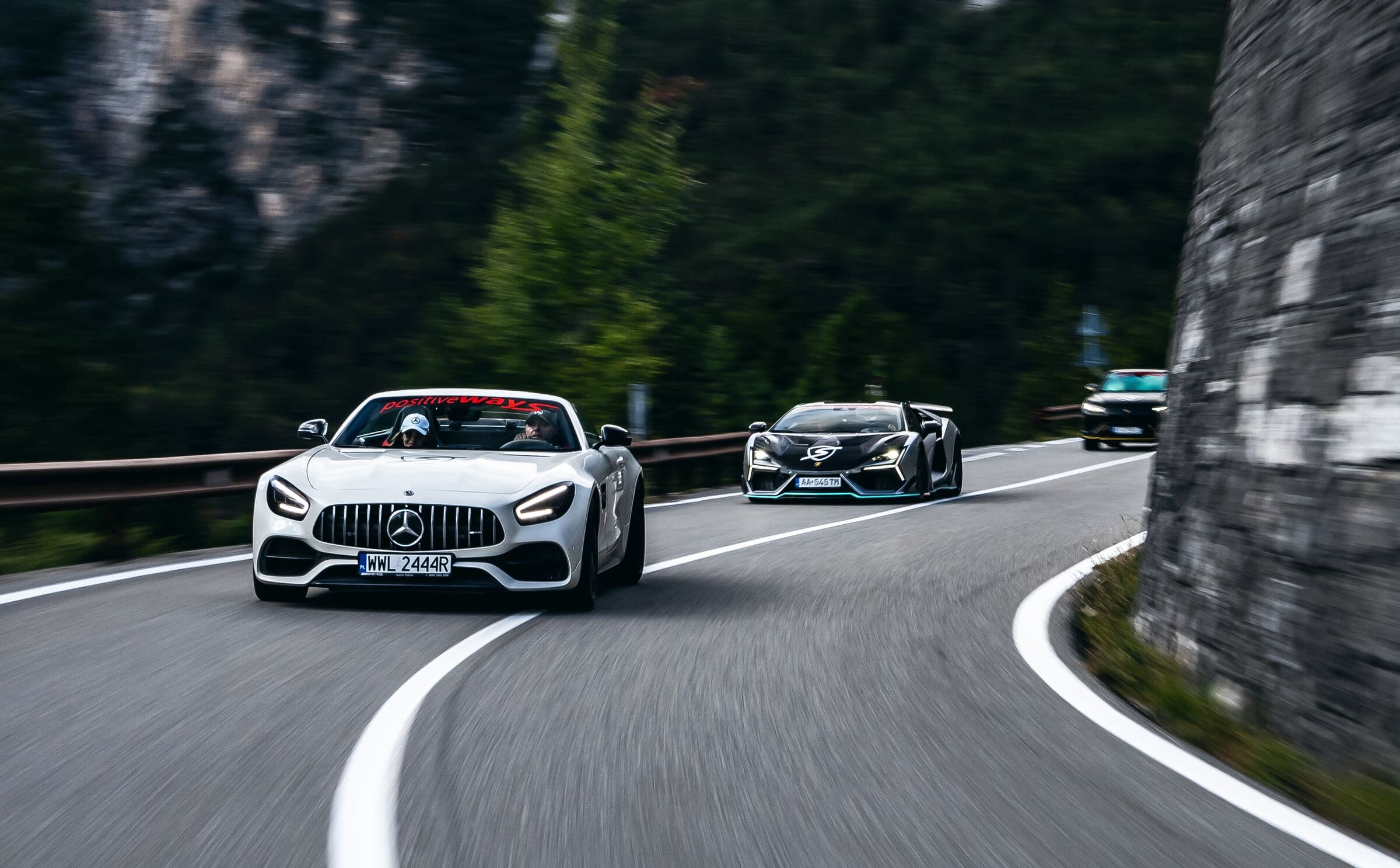 Kolumna aut na alpejskiej serpentynie, na czele srebrny Mercedes